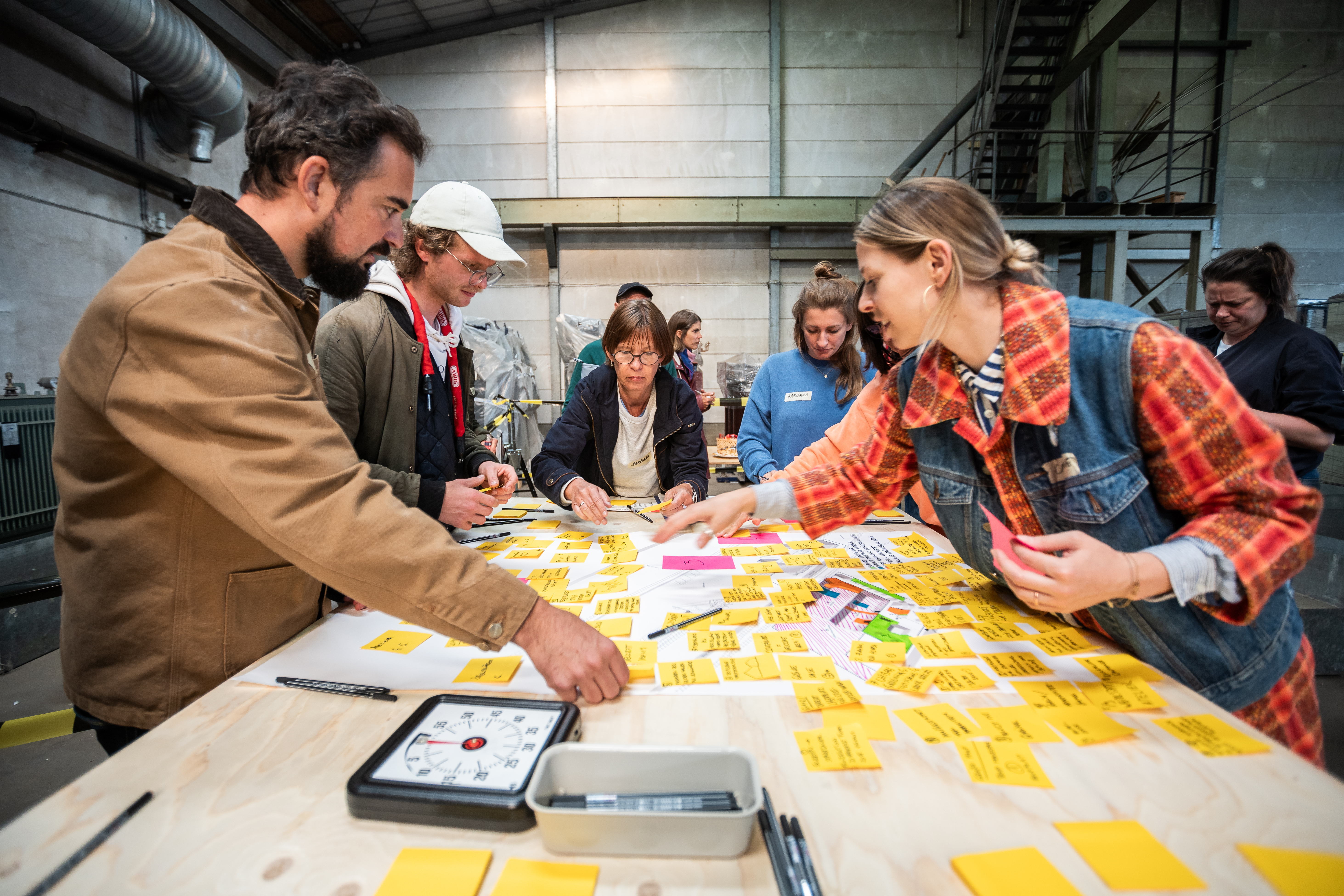 Menschen an einem Tisch arbeiten mit unterschiedlich farbigen Zetteln.