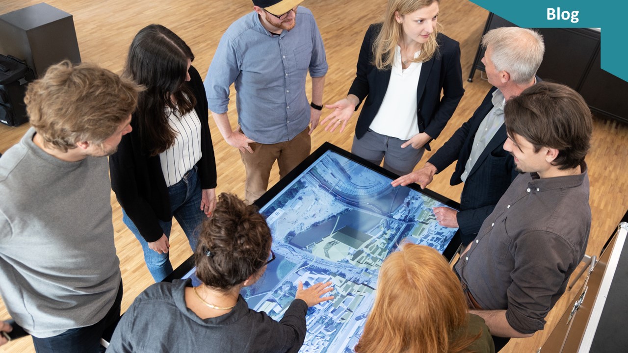 Eine Gruppe von Menschen steht um einen Touchtisch mit einer Stadtplanung.