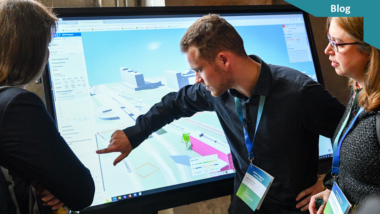 Ein Mann zeigt etwas auf einem großen Bildschirm, auf dem die Umrisse einer Stadt zu erkennen sind. 