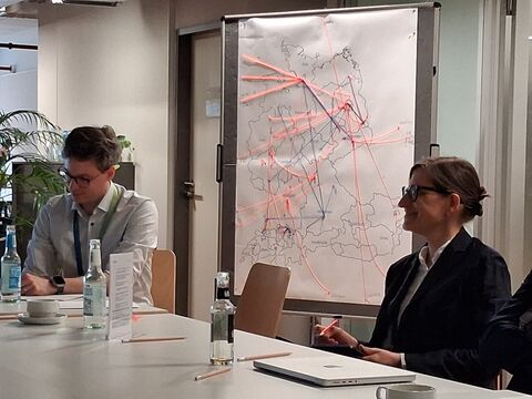 Zwei Menschen sitzen vor einer Stellwand mit Netzwerksimulationen